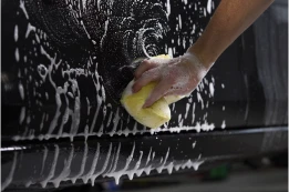 Hand wäscht Auto mit Schwamm und Seifenschaum, Lackfläche ist nass und glänzend.